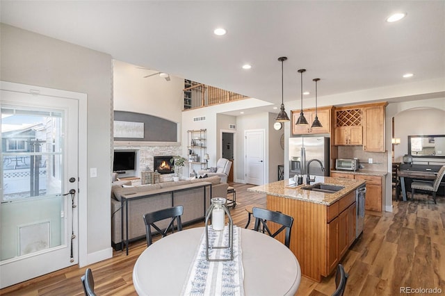 kitchen featuring a sink, appliances with stainless steel finishes, light stone countertops, light wood finished floors, and an island with sink