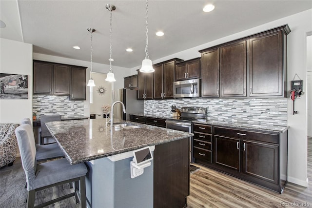 kitchen featuring appliances with stainless steel finishes, a breakfast bar, a sink, dark stone counters, and decorative backsplash