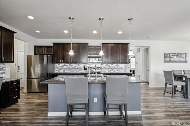 kitchen featuring dark brown cabinetry, backsplash, appliances with stainless steel finishes, dark wood finished floors, and dark stone counters