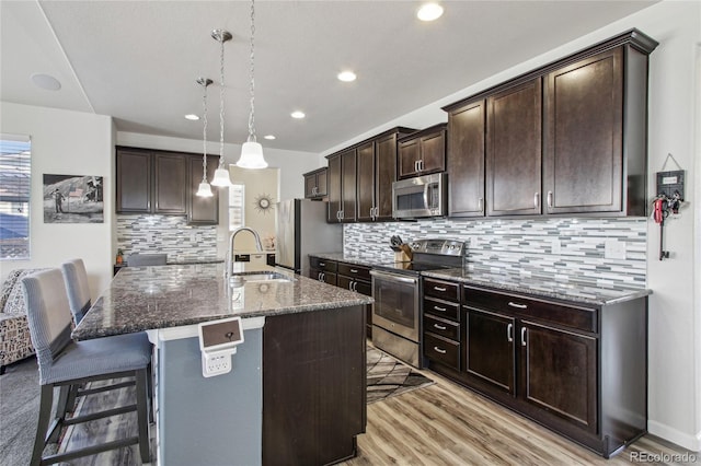 kitchen with backsplash, appliances with stainless steel finishes, a sink, dark stone counters, and a breakfast bar