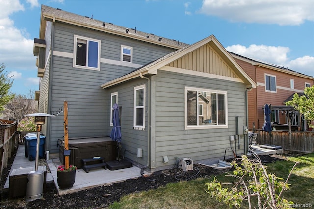 rear view of house featuring a wooden deck, a patio, board and batten siding, and a hot tub