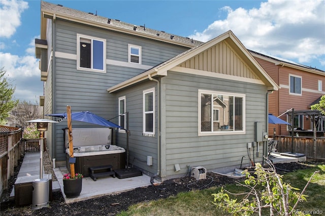 back of property featuring fence, board and batten siding, a hot tub, and a patio area