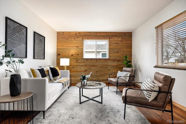 living room featuring wood walls, an accent wall, baseboards, and wood finished floors