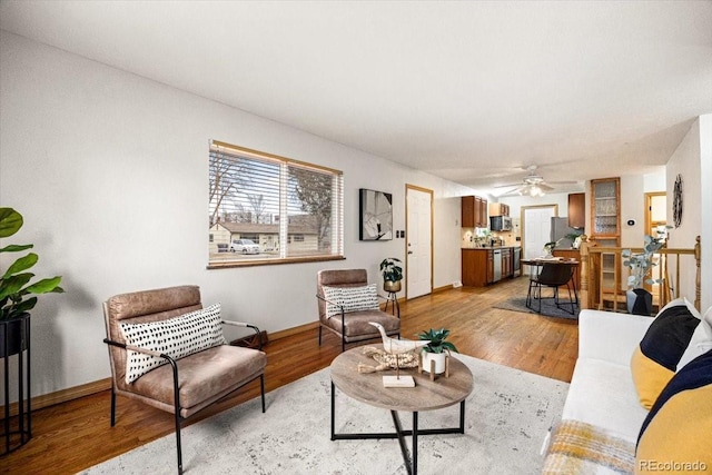 living area with light wood-type flooring, baseboards, and a ceiling fan