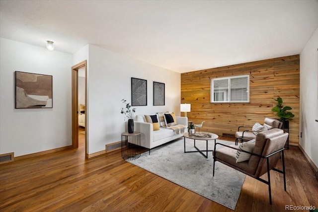 living area with visible vents, baseboards, wood finished floors, and wood walls