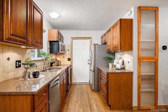 kitchen with light wood finished floors, light stone counters, brown cabinetry, stainless steel appliances, and a sink