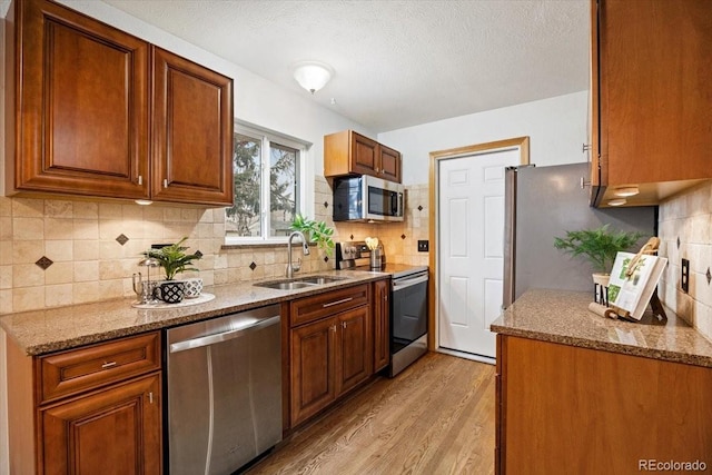 kitchen featuring a sink, light stone counters, backsplash, appliances with stainless steel finishes, and light wood finished floors