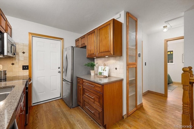 kitchen featuring tasteful backsplash, light stone countertops, light wood-style floors, brown cabinetry, and stainless steel appliances