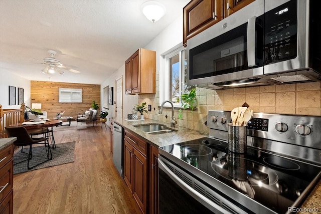 kitchen featuring tasteful backsplash, wood walls, wood finished floors, stainless steel appliances, and a sink