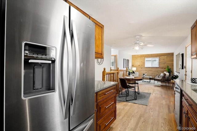 kitchen with a ceiling fan, light stone counters, stainless steel appliances, light wood-style floors, and wooden walls