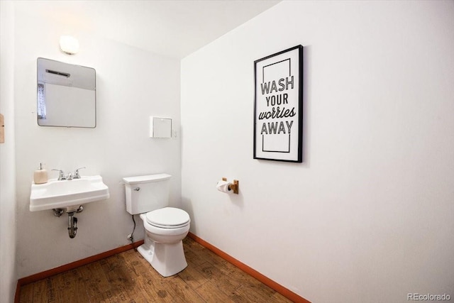 half bath featuring a sink, toilet, baseboards, and wood finished floors