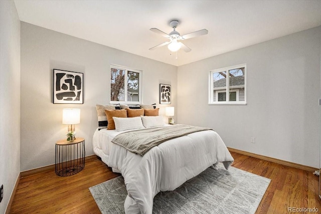 bedroom with a ceiling fan, multiple windows, wood finished floors, and baseboards