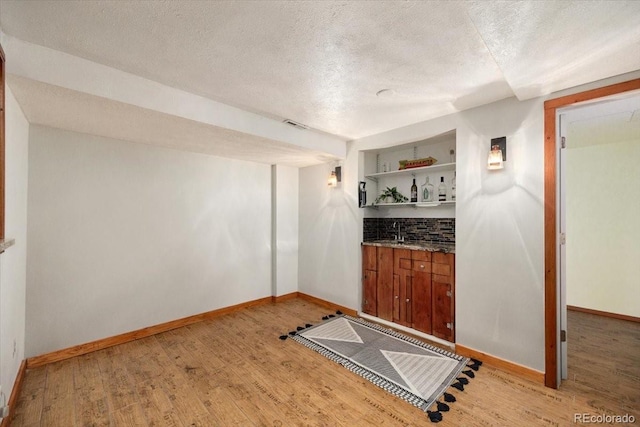 interior space featuring a sink, light wood-type flooring, wet bar, and a textured ceiling