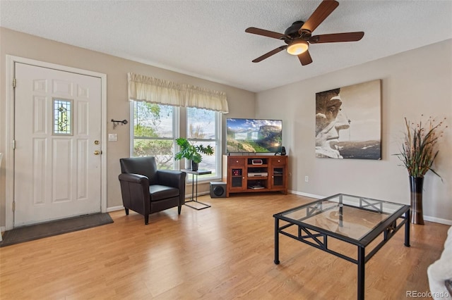 living area featuring a ceiling fan, a textured ceiling, baseboards, and wood finished floors