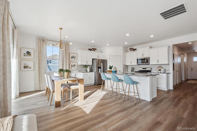 kitchen featuring a center island with sink, light hardwood / wood-style flooring, backsplash, appliances with stainless steel finishes, and white cabinets