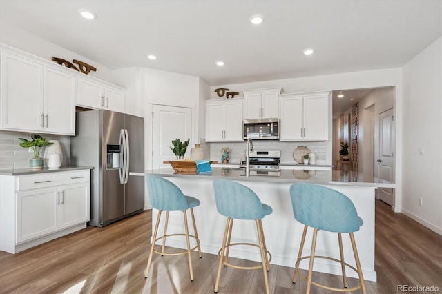 kitchen with an island with sink, appliances with stainless steel finishes, white cabinets, and light wood-type flooring