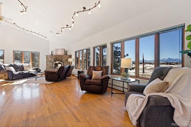 living room featuring a baseboard heating unit, vaulted ceiling, ceiling fan, light wood-type flooring, and a fireplace