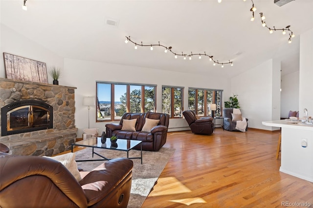 living room with a baseboard heating unit, sink, light hardwood / wood-style flooring, a fireplace, and lofted ceiling