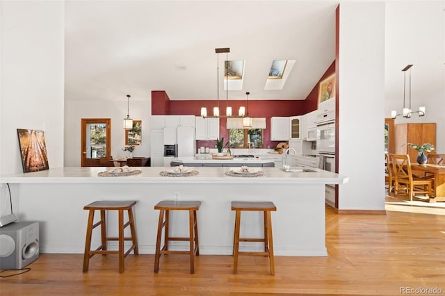 kitchen featuring kitchen peninsula, white cabinets, light hardwood / wood-style floors, white fridge with ice dispenser, and a breakfast bar area