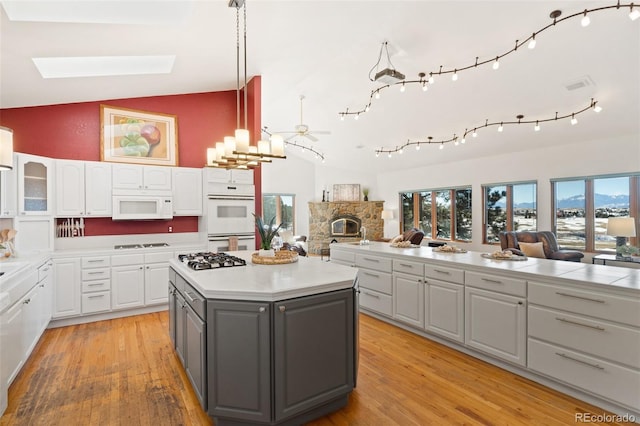 kitchen featuring gray cabinetry, white appliances, white cabinetry, and vaulted ceiling with skylight