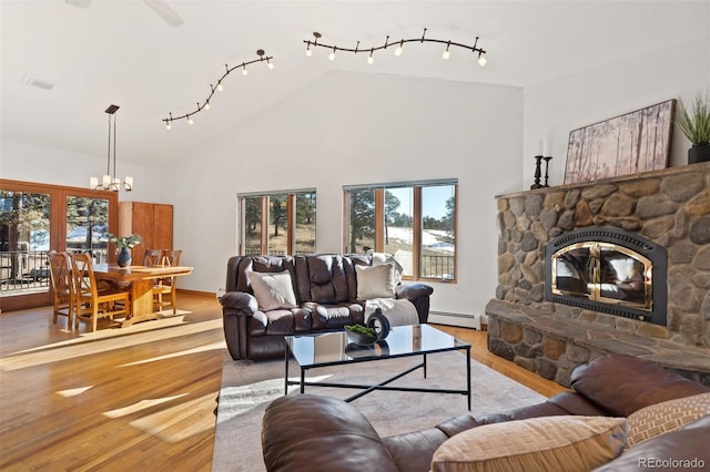 living room with a stone fireplace, high vaulted ceiling, a baseboard heating unit, and light wood-type flooring