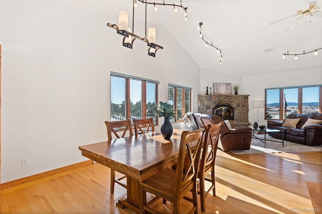 dining space featuring plenty of natural light, light hardwood / wood-style floors, a stone fireplace, and ceiling fan