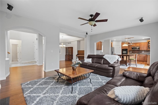 living area with arched walkways, baseboards, light wood-type flooring, and ceiling fan with notable chandelier