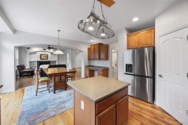 kitchen with a center island, ceiling fan, open floor plan, stainless steel refrigerator with ice dispenser, and arched walkways