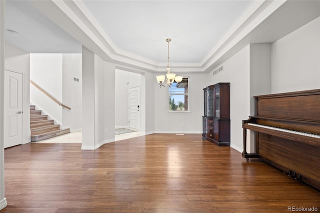 unfurnished dining area featuring a notable chandelier, baseboards, wood-type flooring, visible vents, and a raised ceiling
