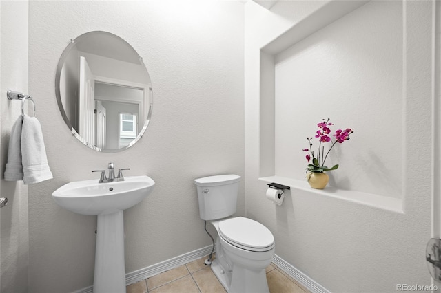half bathroom featuring toilet, baseboards, tile patterned floors, and a sink
