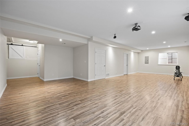 basement featuring electric panel, a barn door, light wood-type flooring, recessed lighting, and baseboards