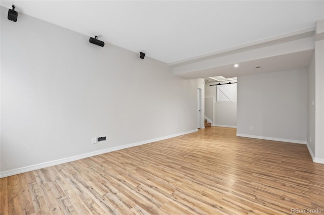 empty room with a barn door, baseboards, and light wood-style floors