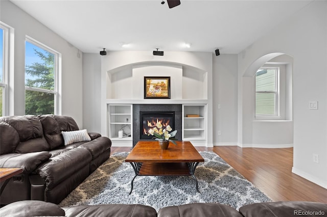 living area featuring wood finished floors, a fireplace, baseboards, arched walkways, and built in shelves