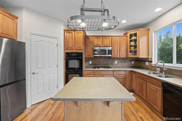 kitchen featuring a sink, tasteful backsplash, black appliances, light wood-style flooring, and glass insert cabinets