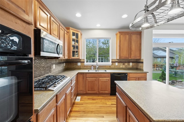 kitchen featuring a sink, decorative backsplash, black appliances, and light wood-style floors
