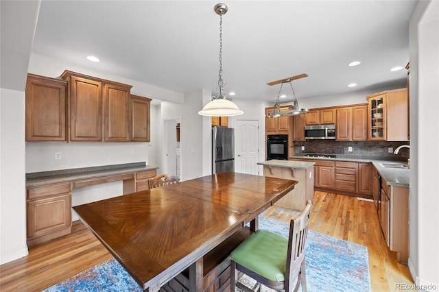 kitchen featuring a sink, tasteful backsplash, light wood-type flooring, glass insert cabinets, and appliances with stainless steel finishes