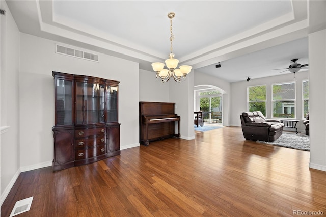 living area with a raised ceiling, arched walkways, visible vents, and wood finished floors