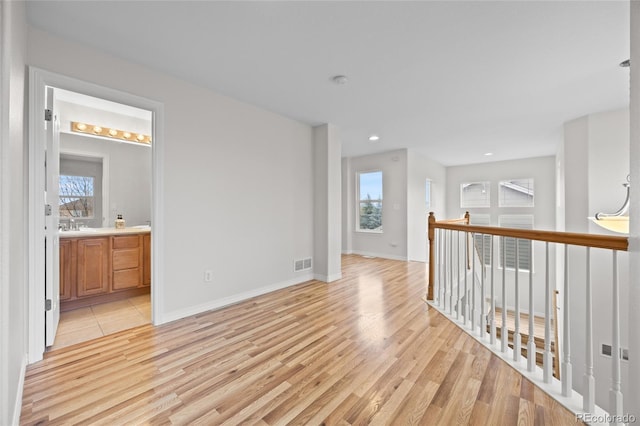 empty room with a sink, light wood-type flooring, visible vents, baseboards, and recessed lighting