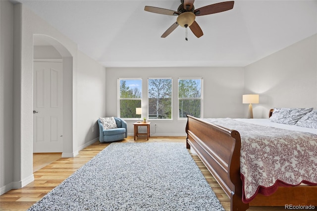 bedroom featuring baseboards, light wood-type flooring, a ceiling fan, and arched walkways