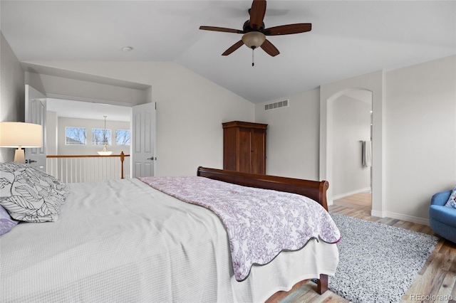 bedroom with lofted ceiling, baseboards, visible vents, wood finished floors, and arched walkways
