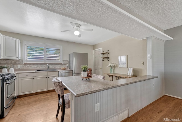 kitchen featuring appliances with stainless steel finishes, a sink, light wood-style flooring, a breakfast bar, and white cabinets