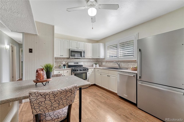 kitchen with stainless steel appliances, a sink, light wood-style floors, backsplash, and a ceiling fan