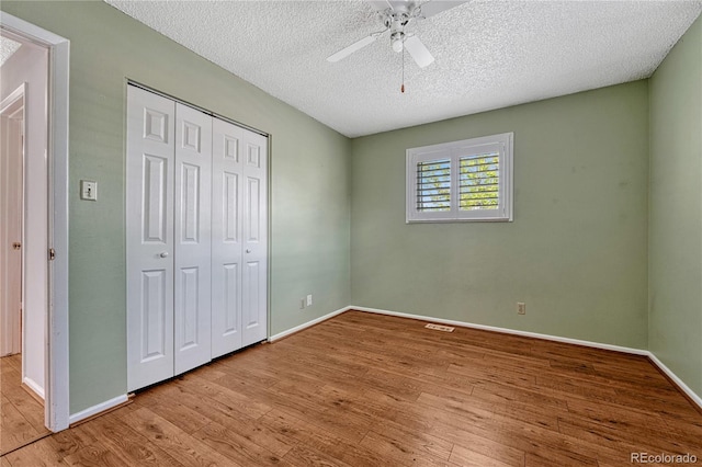 unfurnished bedroom with wood finished floors, a closet, baseboards, a textured ceiling, and a ceiling fan