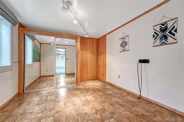 unfurnished room with wooden walls, rail lighting, plenty of natural light, and baseboards