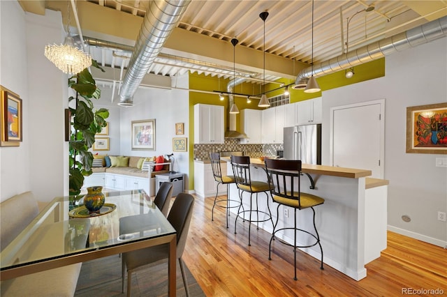 kitchen with a breakfast bar area, high end fridge, backsplash, white cabinets, and decorative light fixtures