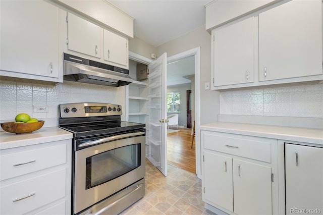 kitchen with stainless steel electric range oven, under cabinet range hood, light countertops, backsplash, and white cabinetry