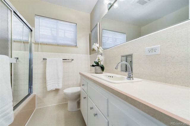 bathroom featuring tile walls, vanity, toilet, combined bath / shower with glass door, and a wainscoted wall
