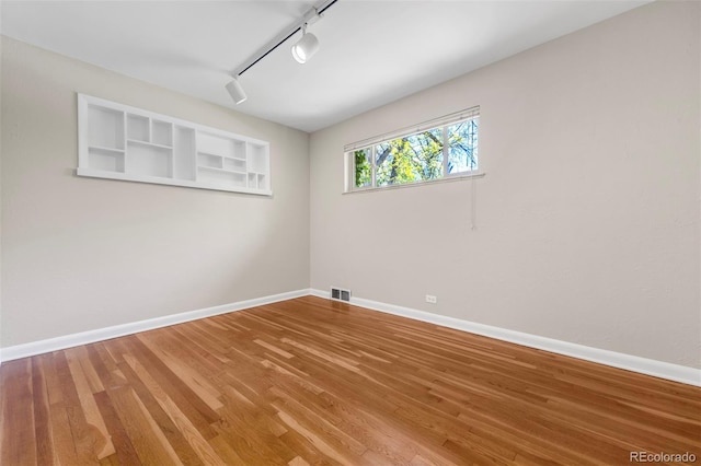 unfurnished room with rail lighting, baseboards, and wood finished floors