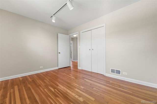 unfurnished bedroom with baseboards, light wood-style floors, a closet, and track lighting
