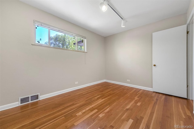 spare room with track lighting, light wood-type flooring, and baseboards